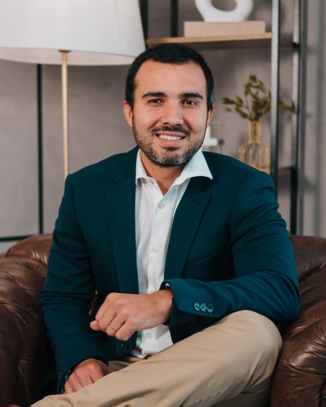 Retrato do Dr. José Fernando, sorrindo, sentado em uma poltrona de couro, de blazer azul-petróleo e camisa branca.